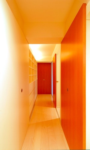 赤い戸と間接照明が白い廊下に奥行きを出す