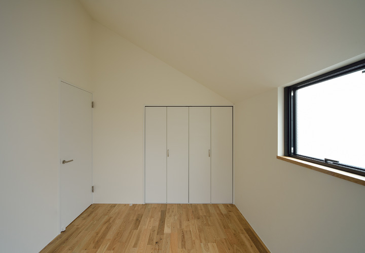 急勾配の屋根面と窓、収納扉の配置が美しい寝室