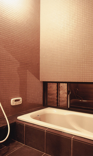 壁面に細かなマットタイル、床面にテクスチャーのある大きめのタイルを使用した、落ち着いた浴室