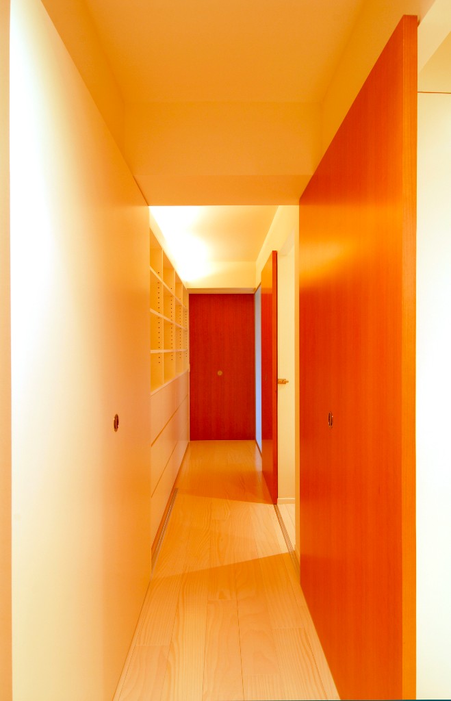 赤い戸と間接照明が白い廊下に奥行きを出す