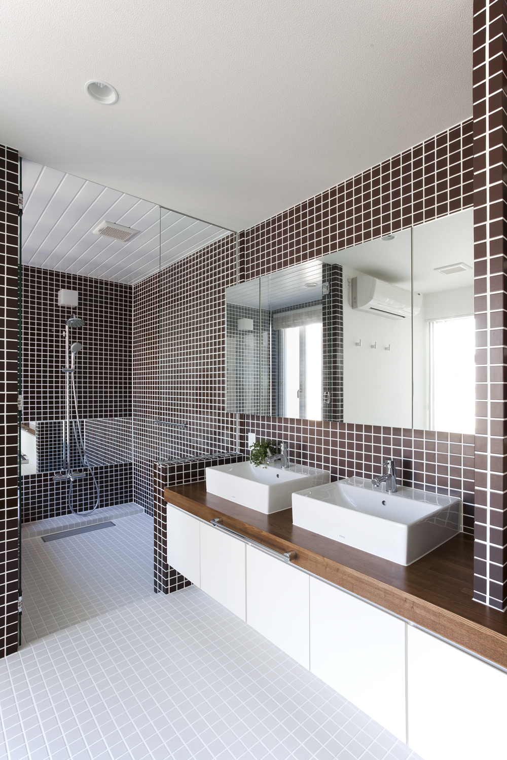 浴室との仕切りガラスが空間に狭さを感じさせない、茶色のタイルが印象的な洗面所