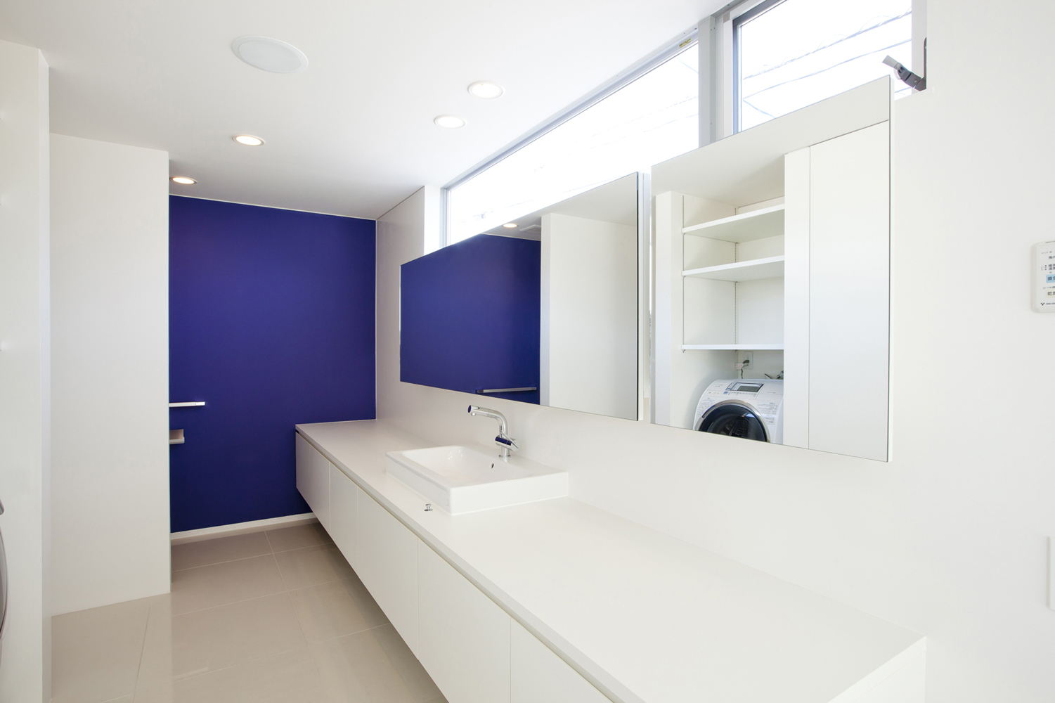 白の空間に彩度の高い青色の壁が、生活感を感じさせない洗面所