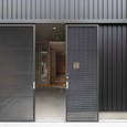 細身のエキスパンドメタル親子吊戸。普段は大きい戸を固定し小さい戸のみ開閉。自転車やバイクの出し入れ時は大小の戸を控壁へ収めて全開放。