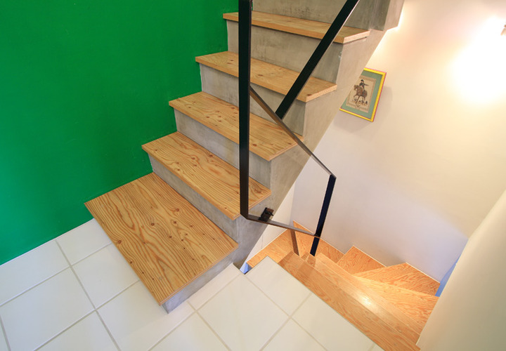 ビビッドなグリーンの壁に調和する階段のナチュラルな踏み板と黒い手すり