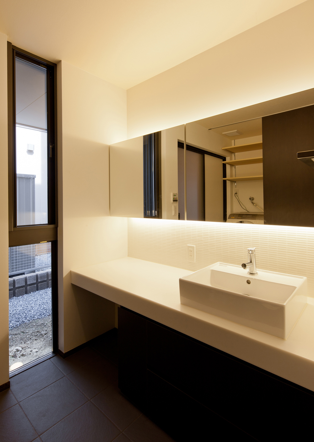 間接照明の柔らかい光と焦げ茶色のタイルが、落ち着いた雰囲気のある洗面空間に