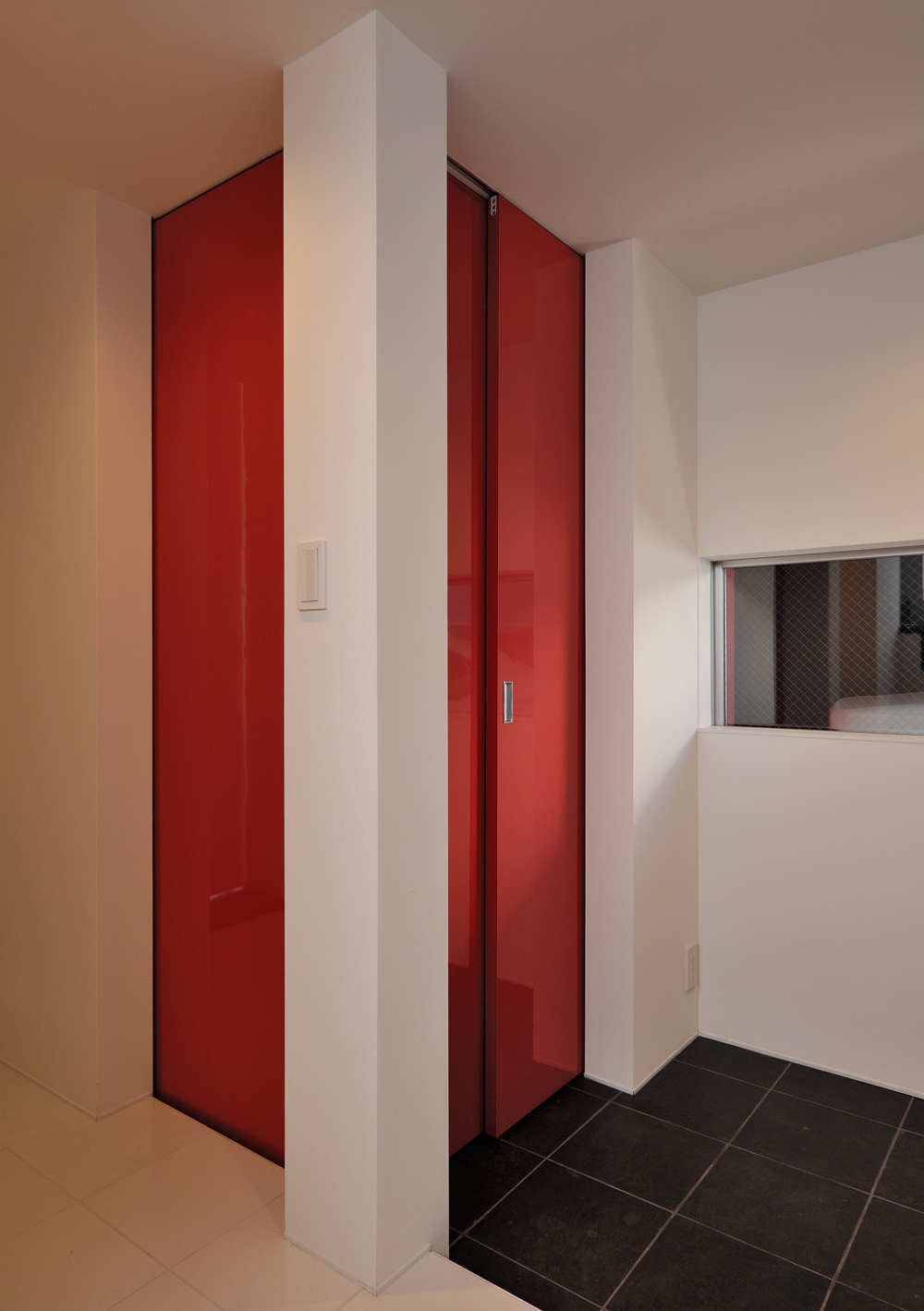 白と黒のタイルの床材に、この家のシンボルカラーの赤色の扉が個性的な玄関ホール