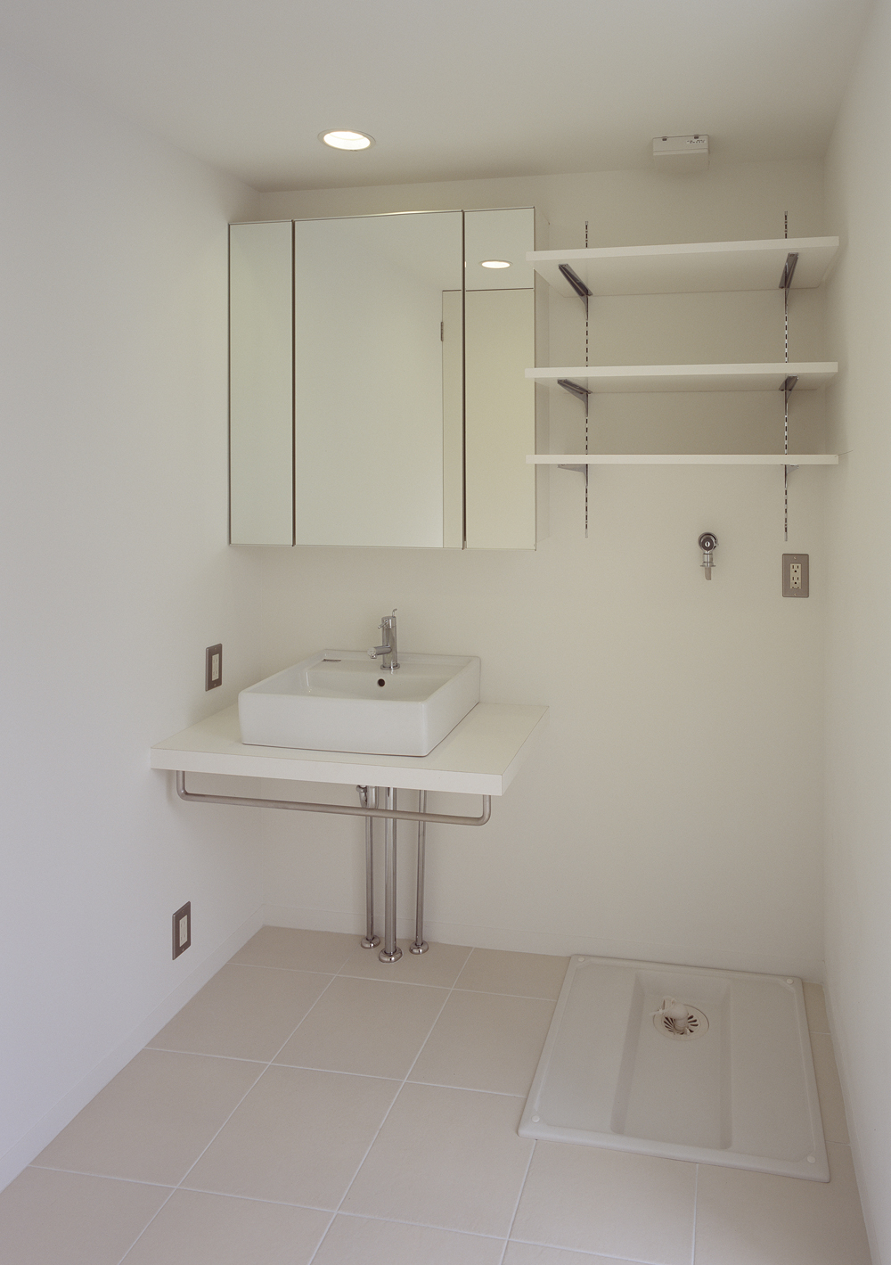 バスルームと同じ白い床タイルを使用した、コンパクトにまとめた洗面所