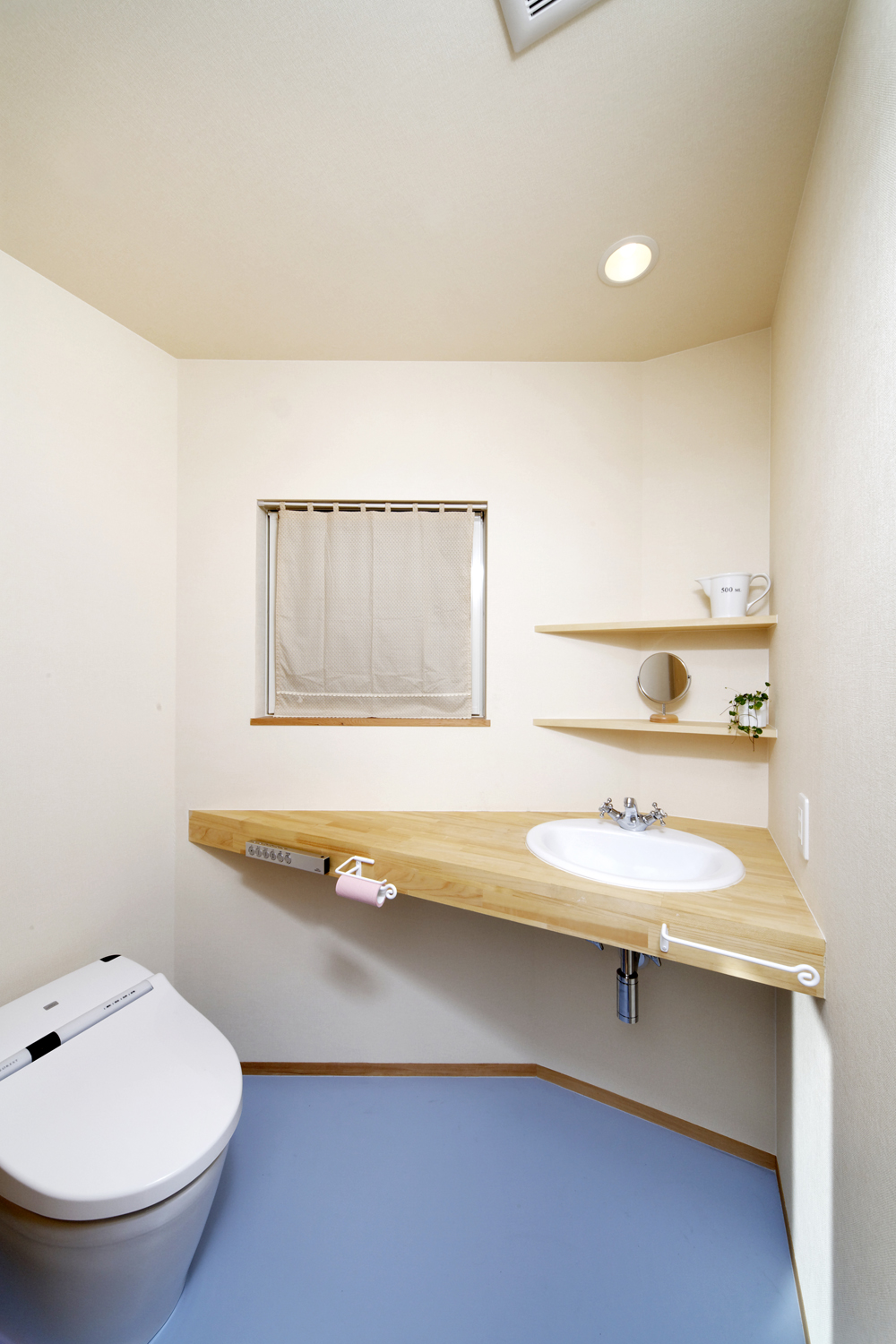 変形型の空間に角を有効活用した、水色の床がかわいらしいトイレ