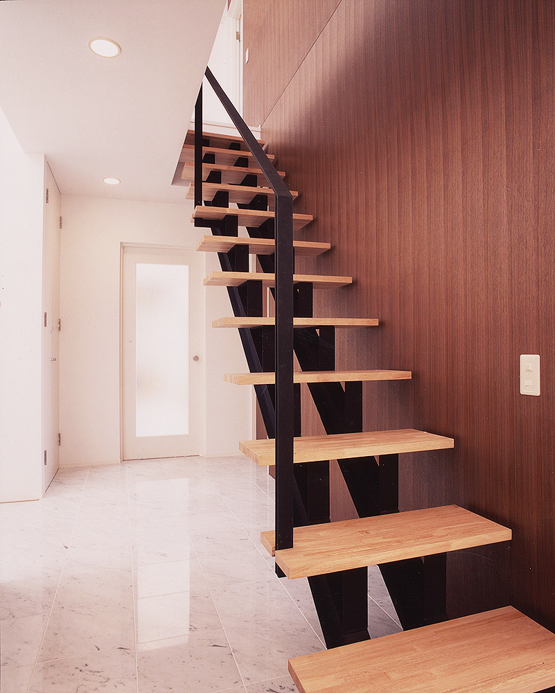 黒と木調でまとめた階段周りを上品にまとめる、階段ホールの白い石調タイル