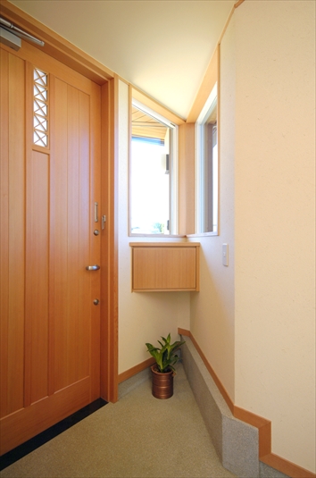 敷地に従った形状の玄関平面と木製建具のドア